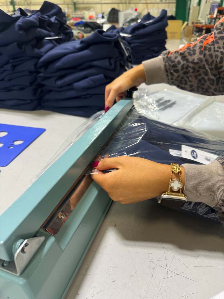 An ATS team member sealing a poly-bagged garment at the packing bench
